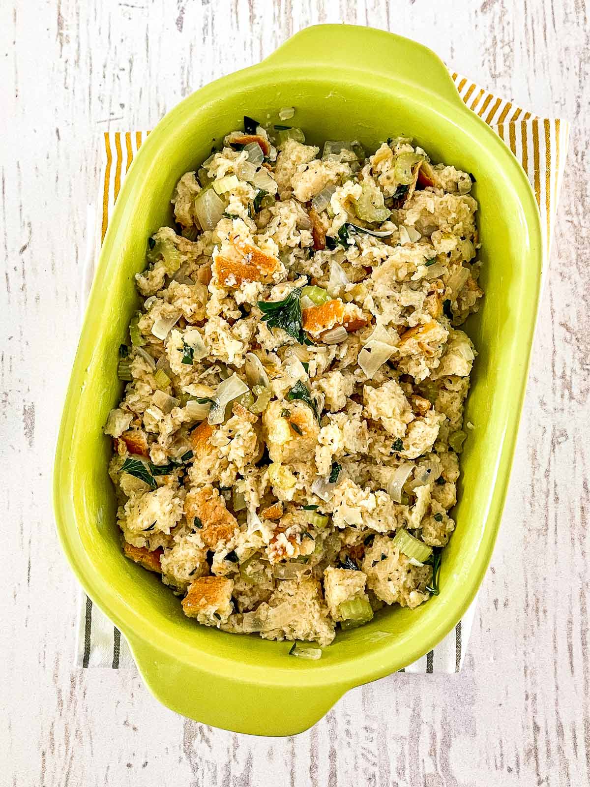 Green casserole dish with the uncooked stuffing mixture ready to bake.