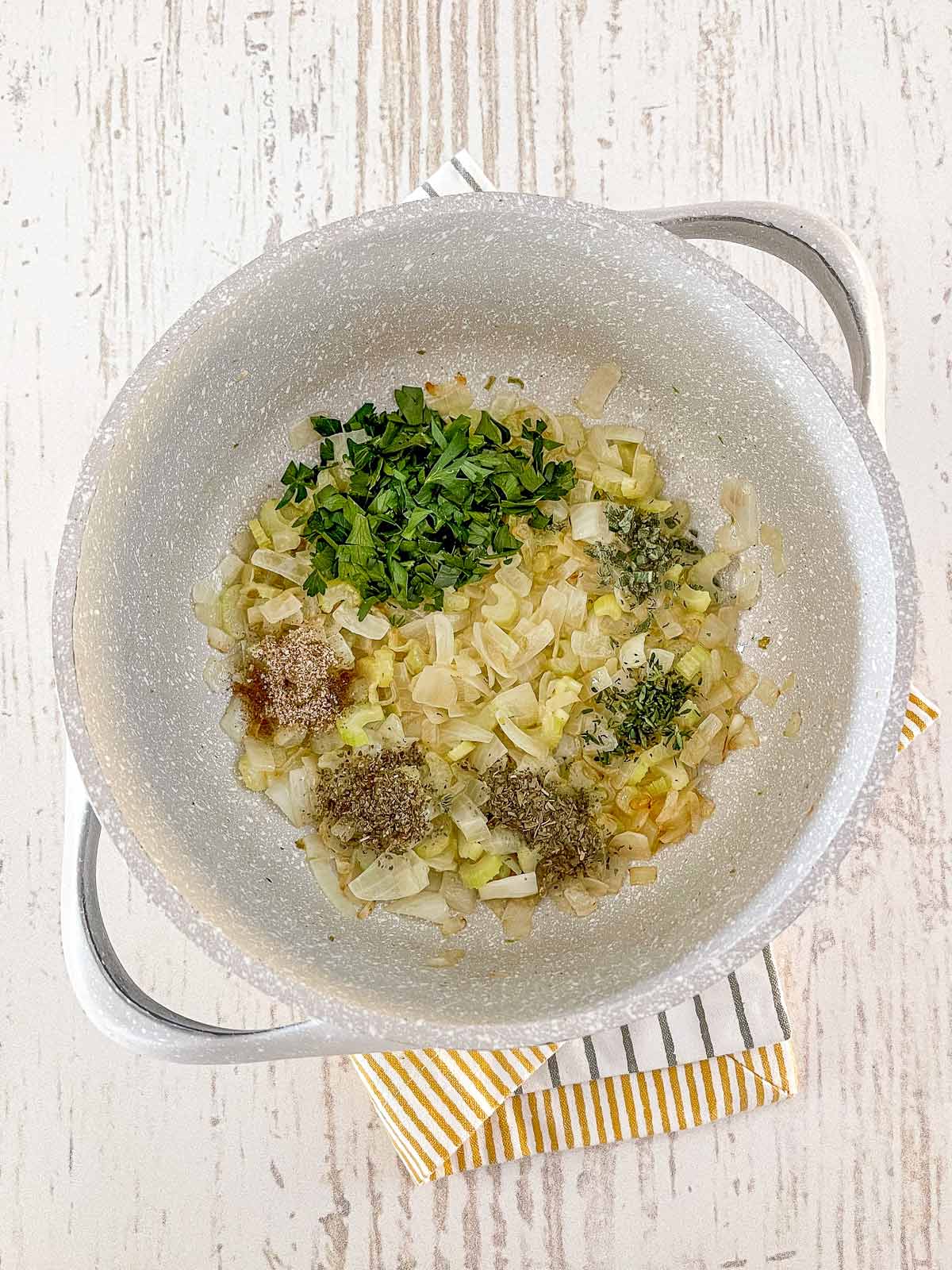 Pot with cooked onions and celery wilth spices and fresh herbs added.