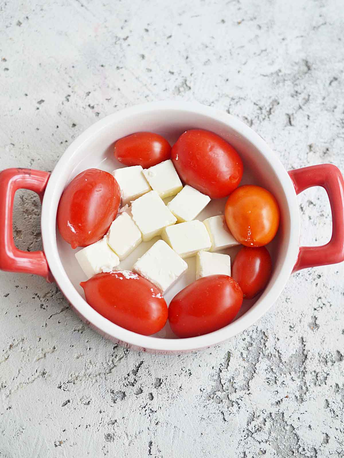 Baking pan with cherry tomatoes in a circle around feta cheese in the middle.