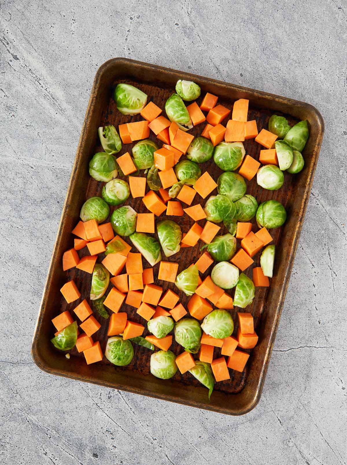Baking sheet of raw sweet potatoes and Brussels sprouts.