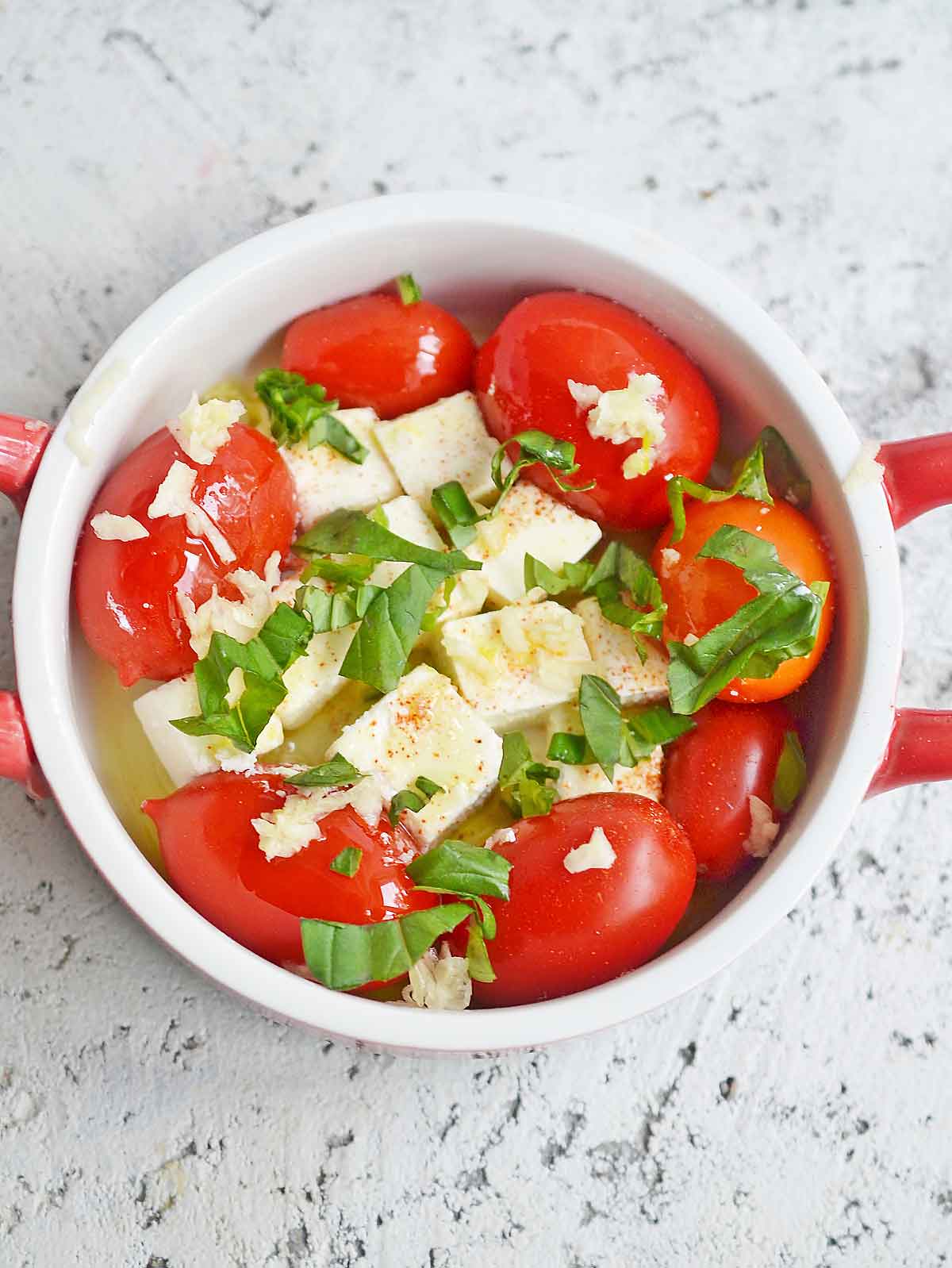 Cherry tomatoes, and feta in a baking dish with oil, wine, salt, pepper, garlic, and basil.