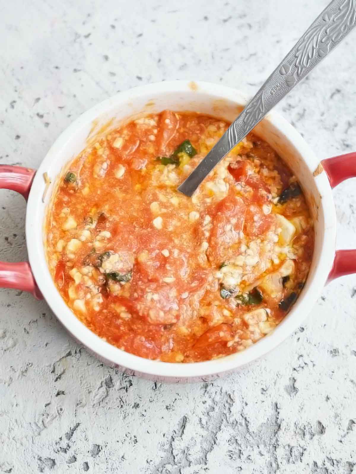 Cooked tomatoes and feta mixed up with a fork.