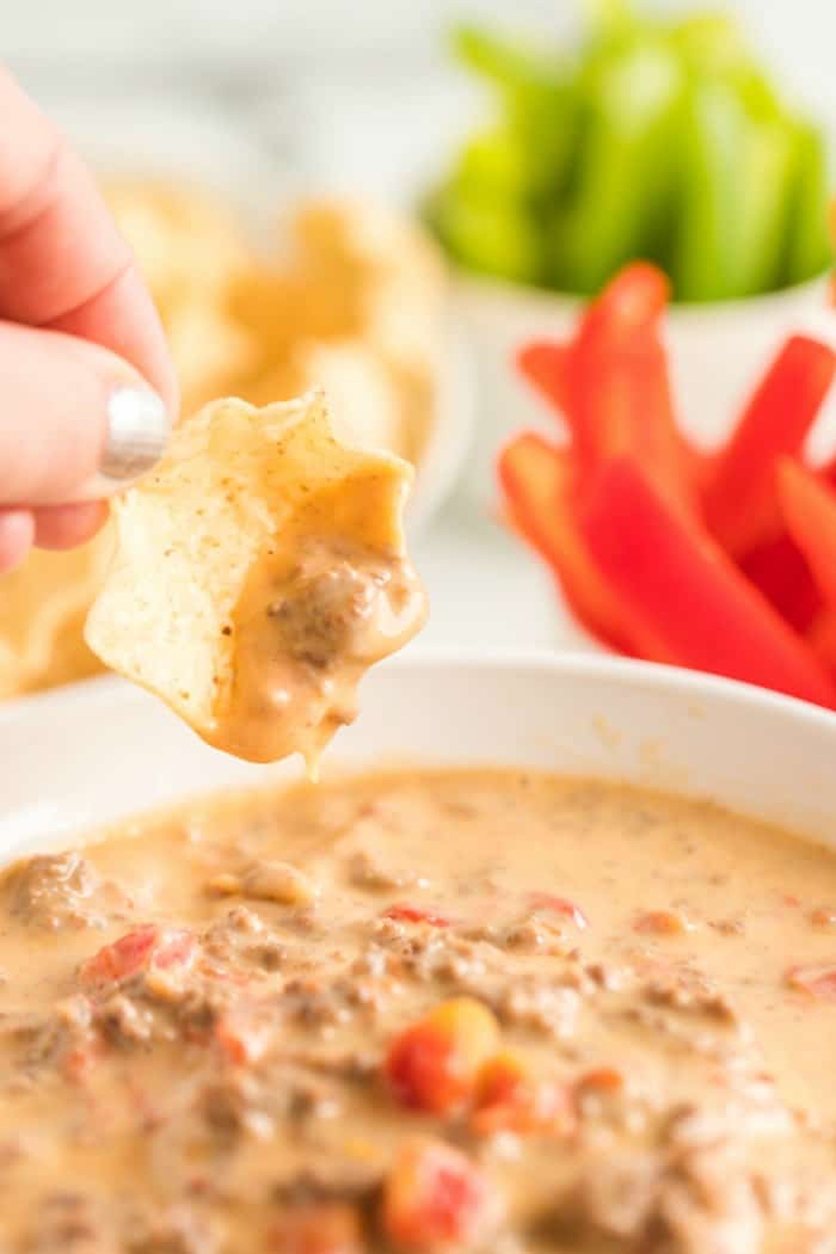 A bowl-shaped chip is dipped into a melty cheese dip.