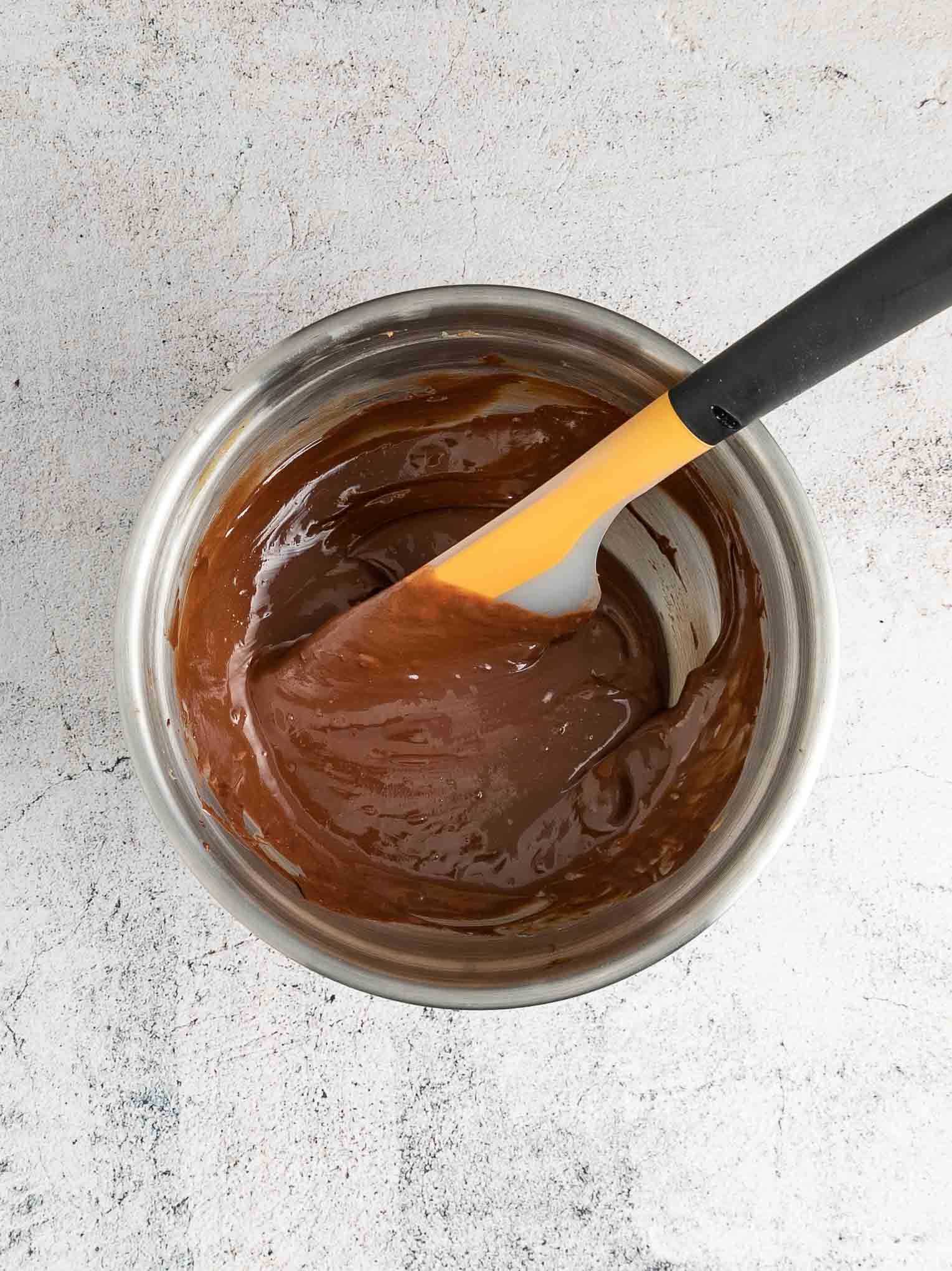 Melted chocolate chips, peanut, and butter in a mixing bowl with spatula.