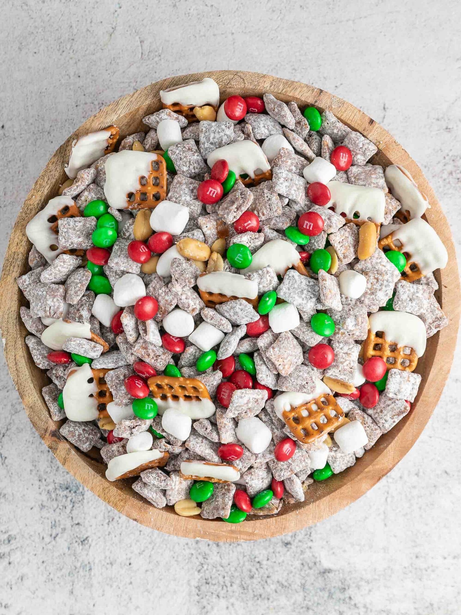 Muddy Buddies in a wooden bowl with M&M's, peanuts, mini marshmallows, and pretzels.