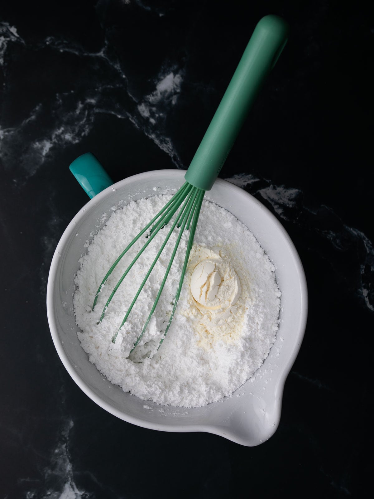 Mixing bowl with powdered sugar and meringue powder, and water.