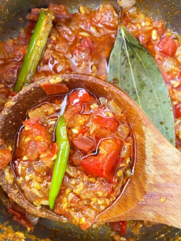 Green chilies are added to the pot with spices and garlic and onion.