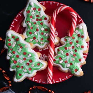 Small red plate with decorated Christmas tree cookies and a candy cane.