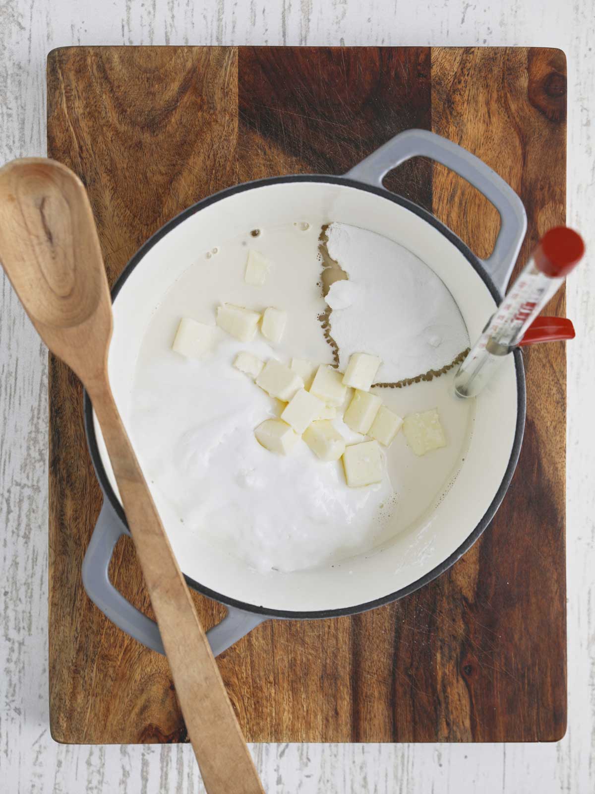 Heavy pot with ingredients plus wooden spoon and candy thermometer.