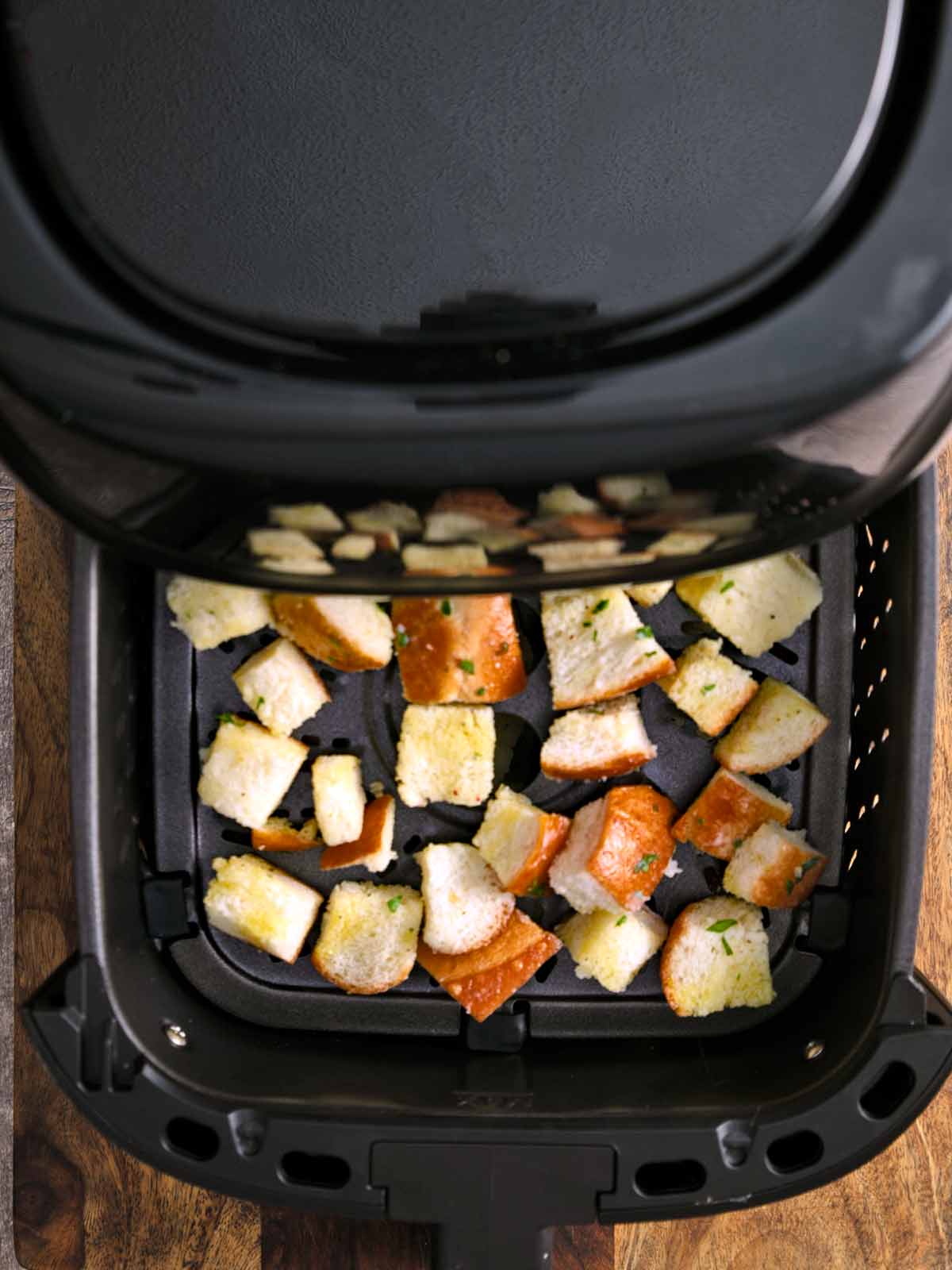 Toasted bread cubes being pulled out of the air fryer.