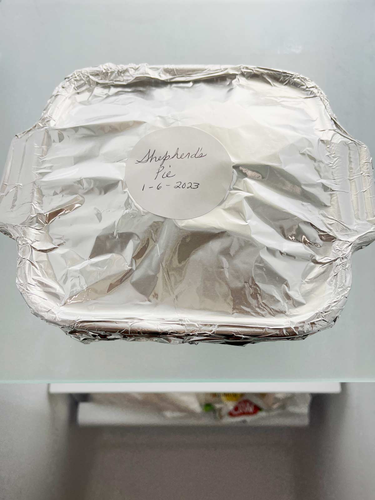 Small baking dish with aluminum foil over top and label on top, in the freezer.