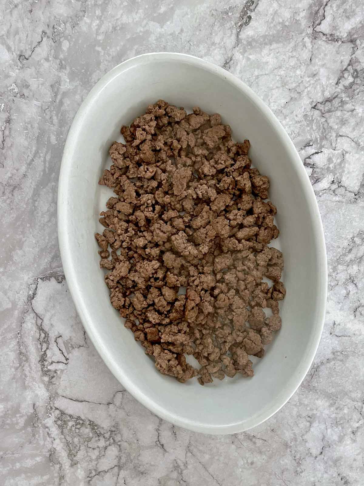 Ground beef in a small oval casserole dish.