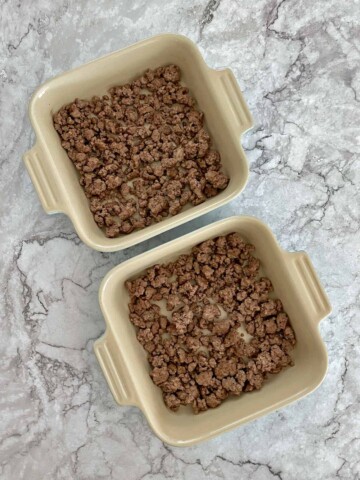 Two small baking dishes with ground beef on the bottoms.