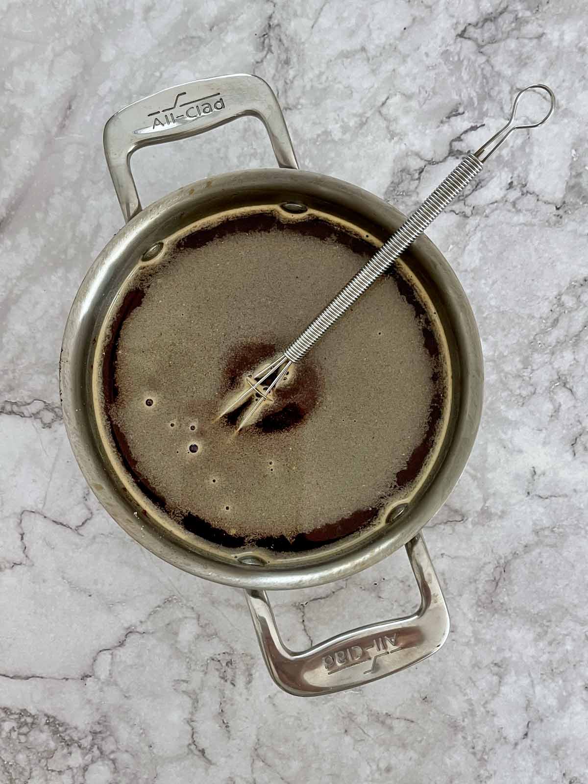 Small pot with brown gravy and whisk.