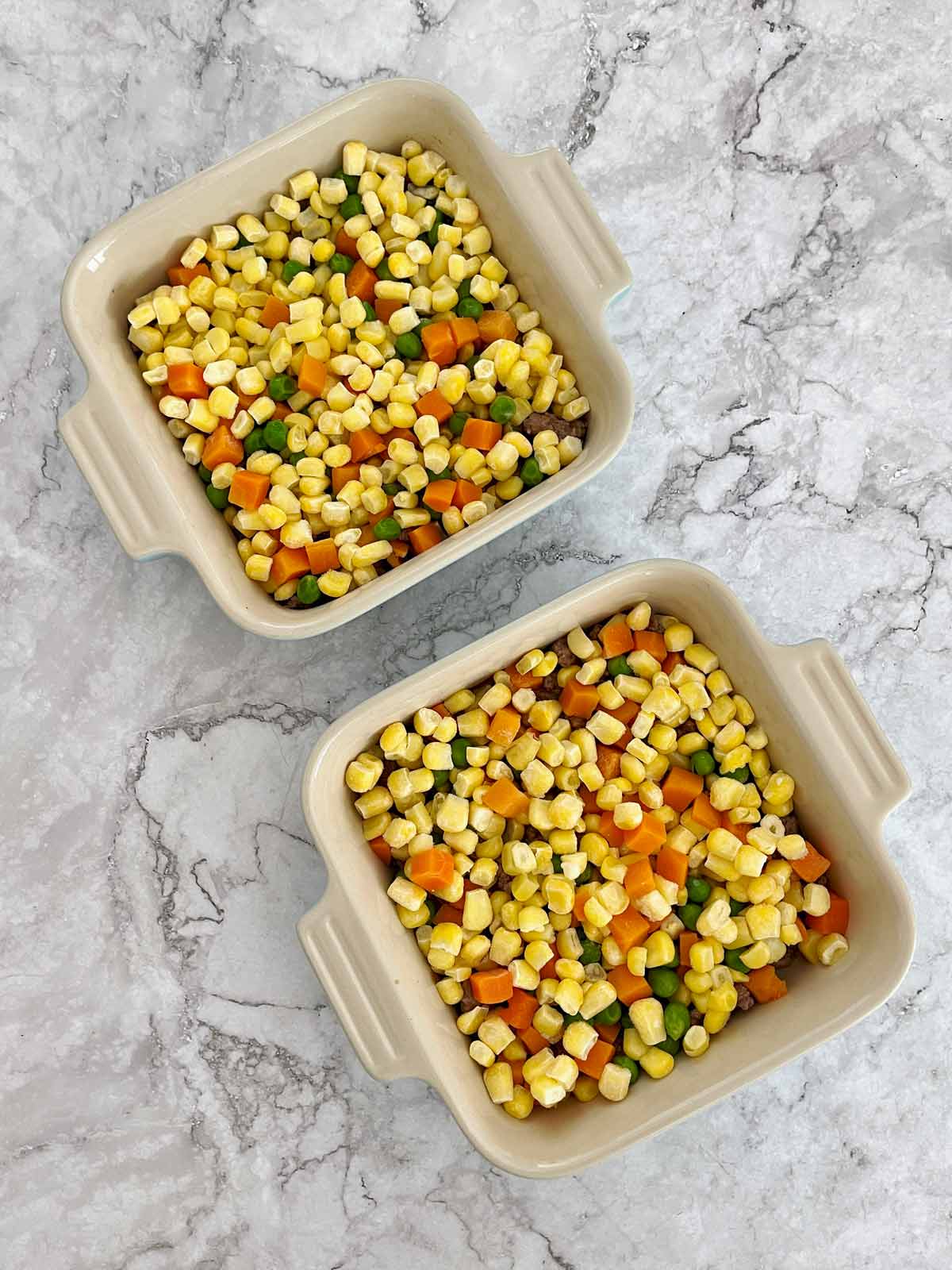 Baking dishes with mixed vegetables on top of meat.