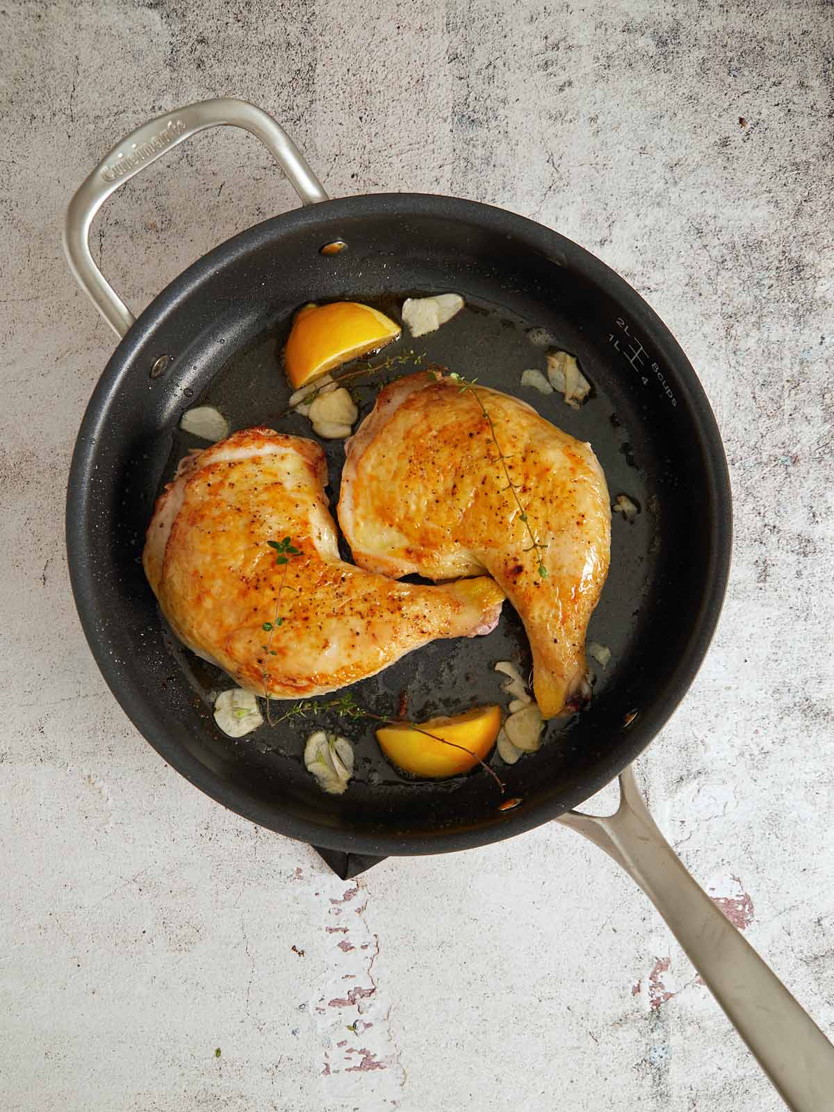Brick removed to show chicken flipped skin aide up and golden brown. lemon chunks and garlic added to skillet.