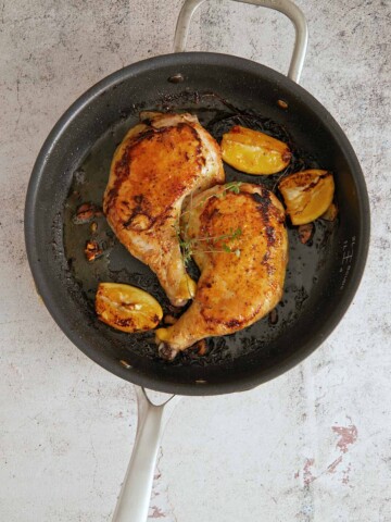 Fully cooked chicken pieces in the skillet with cooked down lemons and golden brown garlic slices.