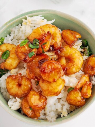A plate of cooked white rice with sticky sauced shrimp.