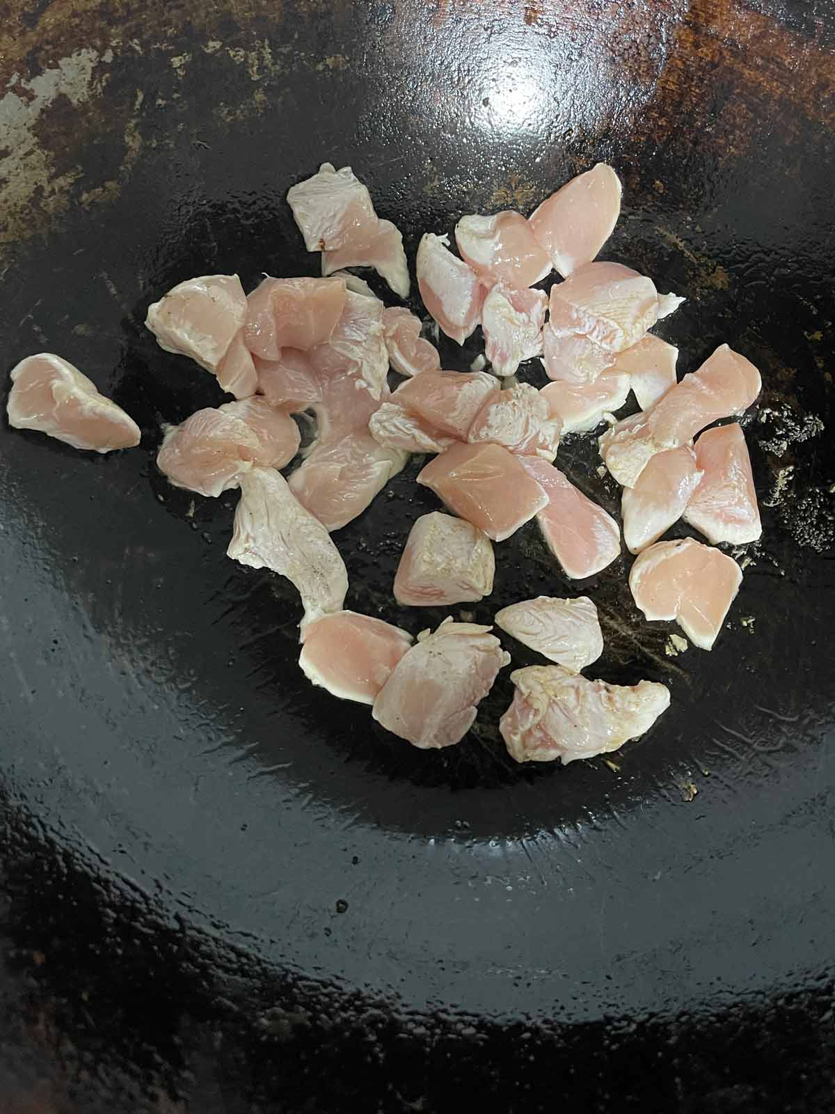 Chicken added to a hot wok in a single layer.
