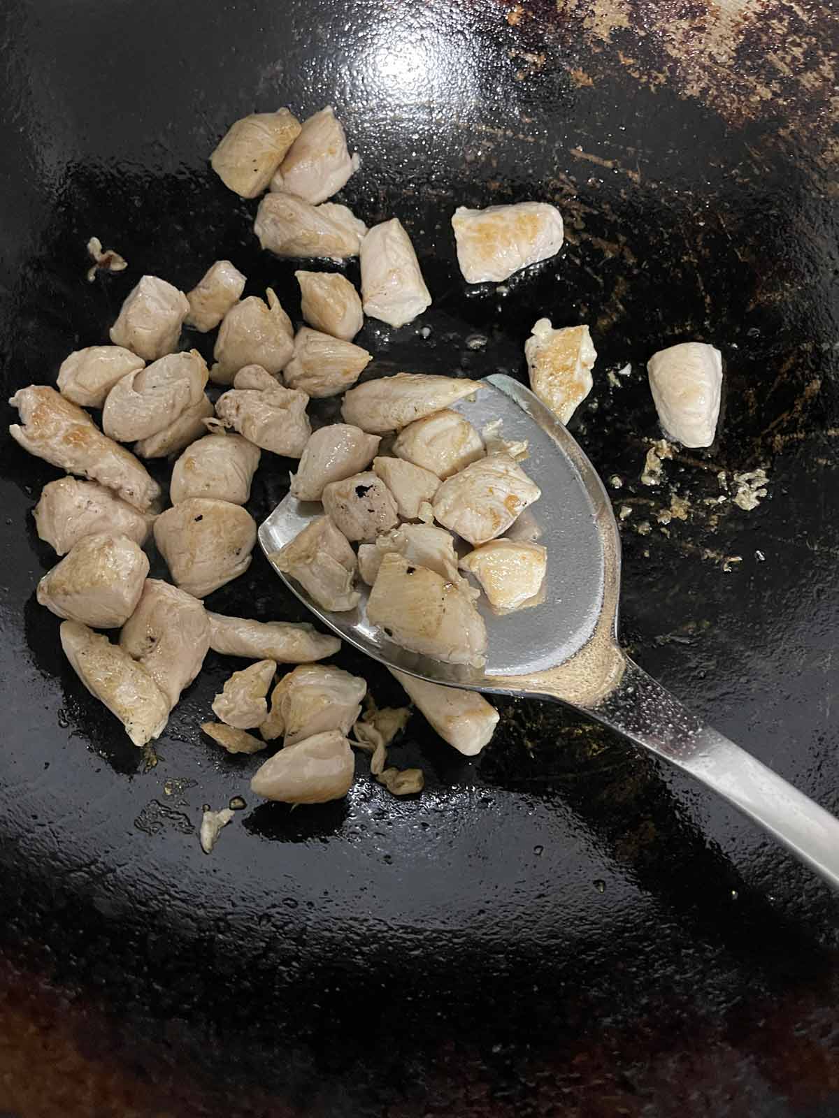 Chicken being stir fried in a wok.