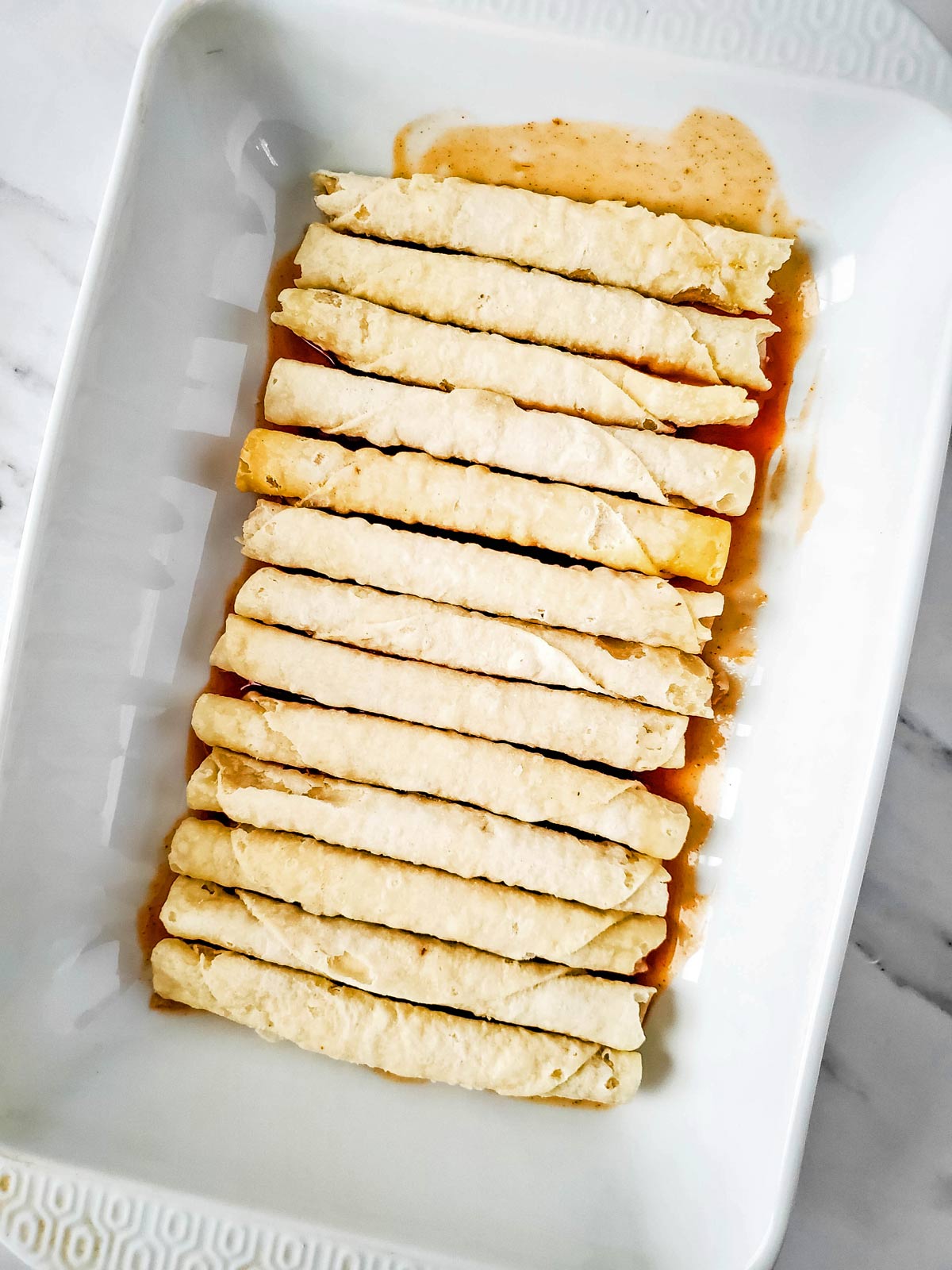 Frozen Taquitos in casserole dish on top of enchilada sauce.