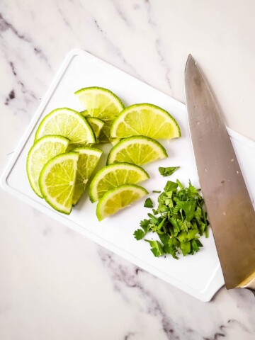 Cutting board, knife, lime slices. and chopped cilantro.