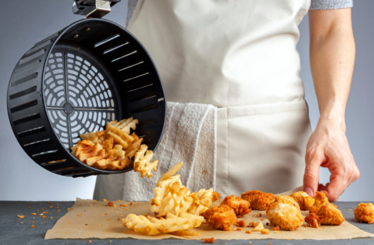 Cook pouring crispy air-fried potatoes out of the air fryer basket.