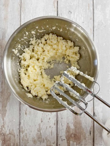 Sugar and butter mixed in a large bowl with handheld electric mixer.