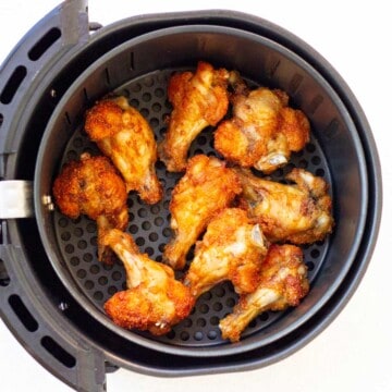 Basket of air fryer with cooked chicken wings.