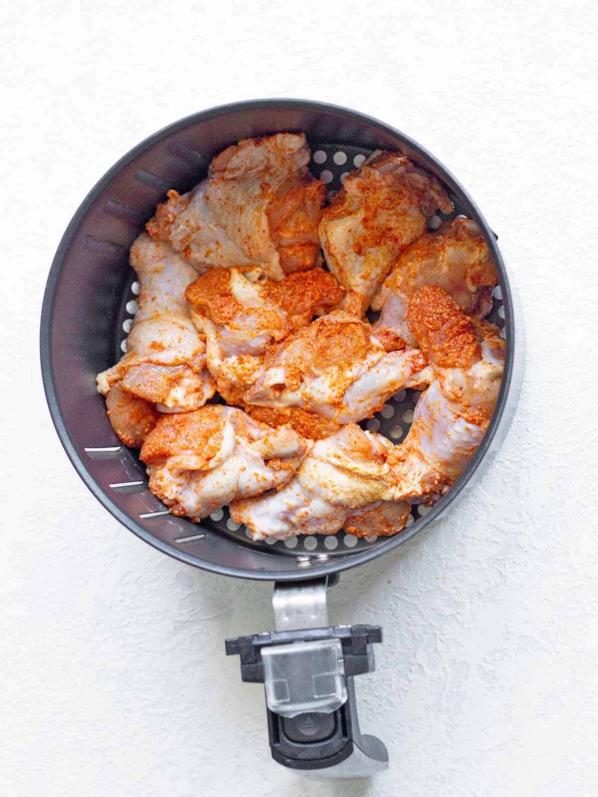 Single layer of seasoned chicken wings in the air fryer basket, ready to cook.