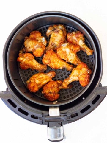 Fully cooked, golden brown chicken wings in the air fryer basket.

