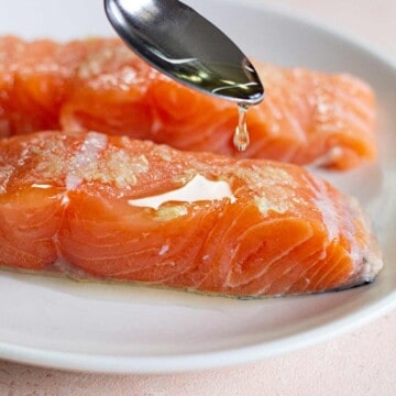 Salmon with oil being drizzled on with a spoon.