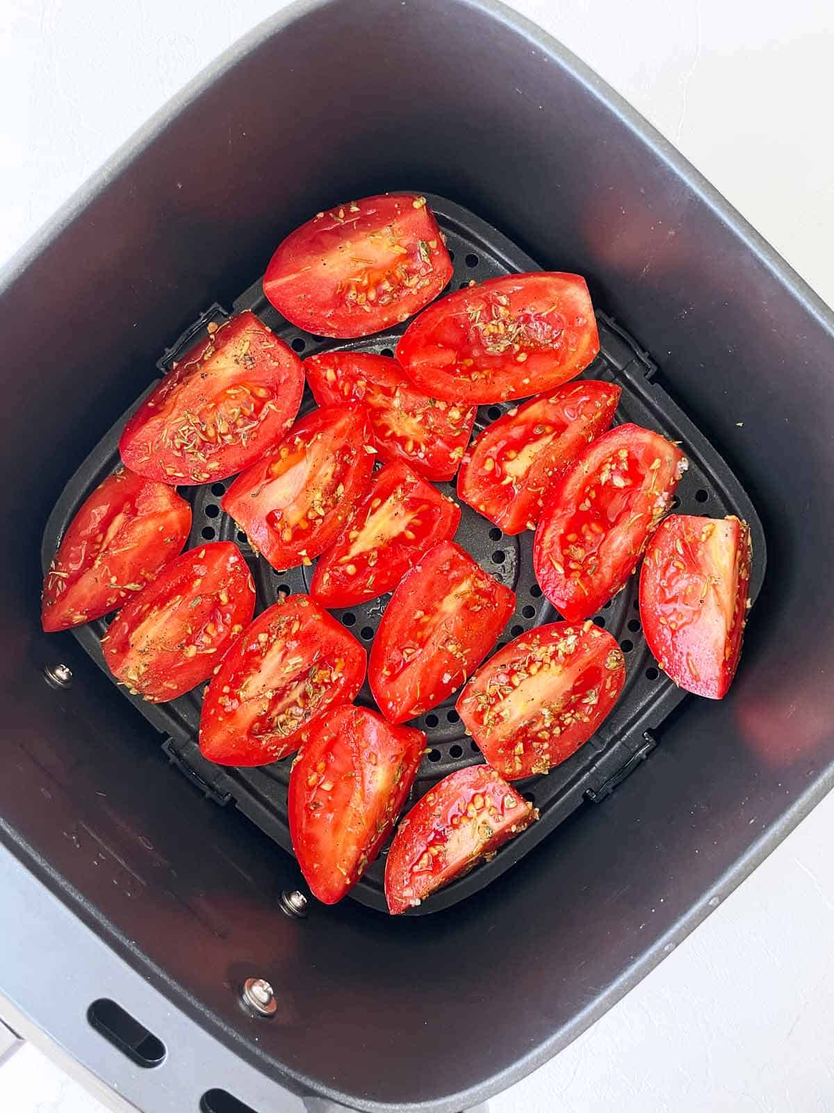 Seasoned tomatoes in the air fryer tray in single layes.