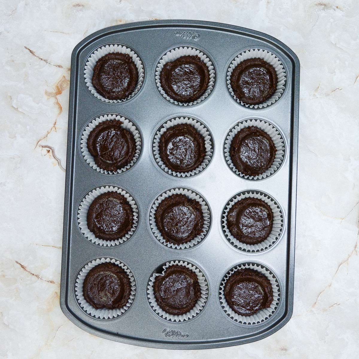 12 hole cupcake tin with paper liners and brownie batter.