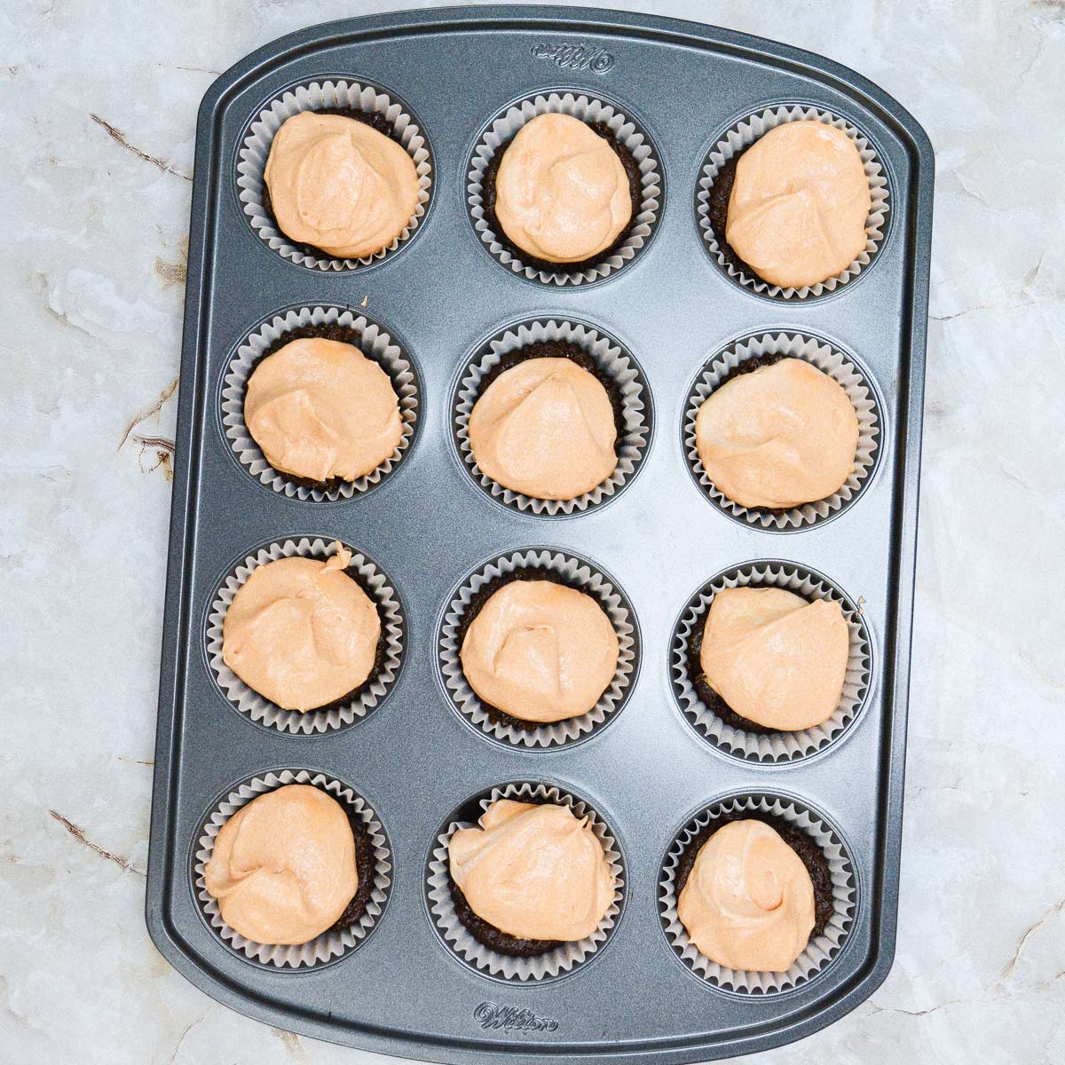 12 hole cupcake pan with cake batter on top of brownie layer.