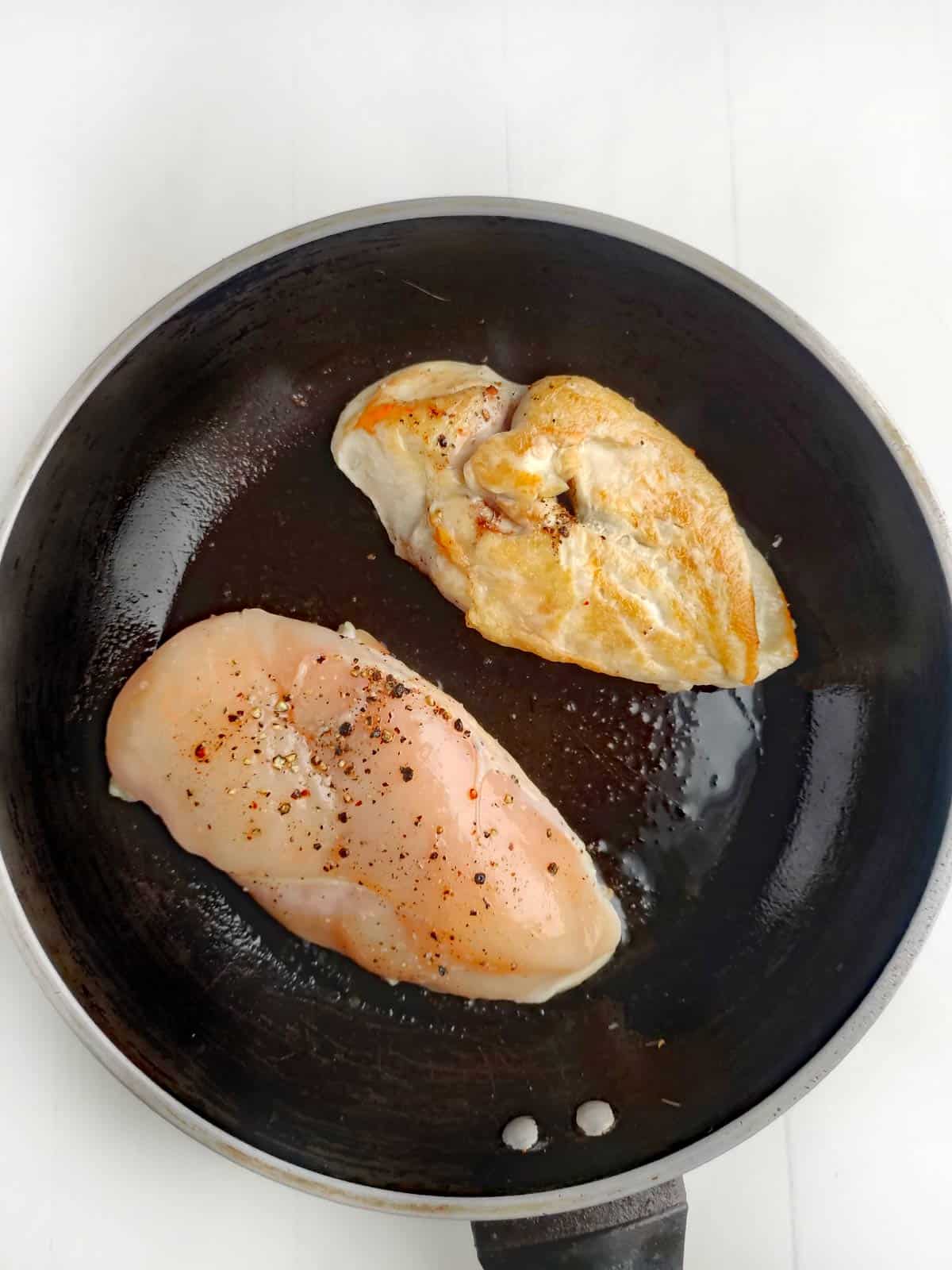 Two chicken breasts browning in a non-stick skillet.