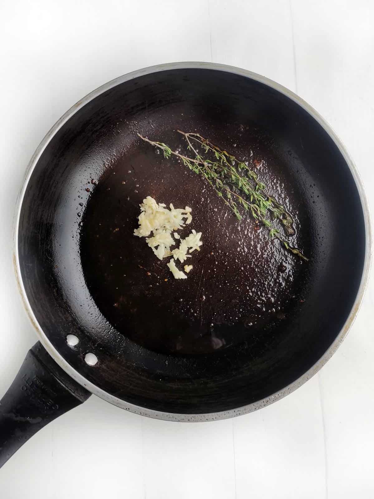 Non-stick skillet with garlic and thyme cooking.