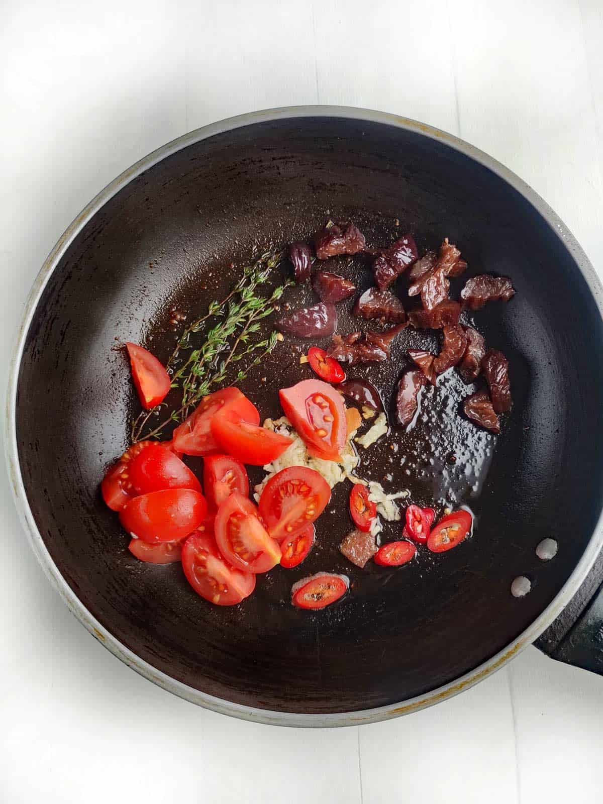Non-stick skillet with thyme, garlic and tomatoes cooking.