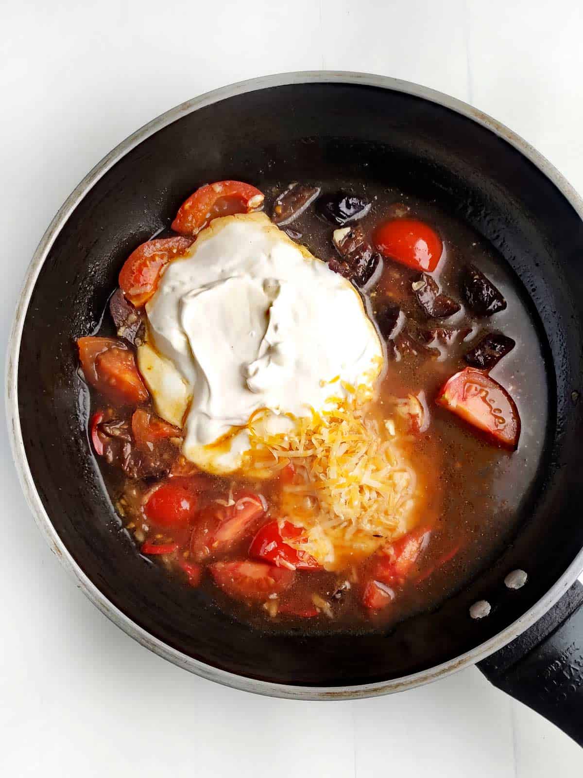Sour cream and grated cheese in the skillet with spices, herbs, and tomatoes.