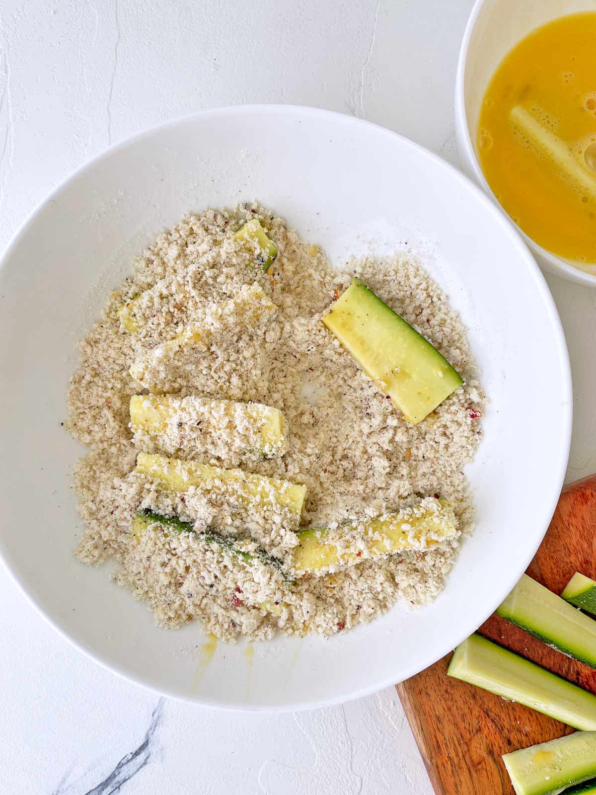 Bowl with zucchini strips getting covered in breadcrumbs.