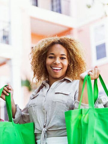 Smiling lady lifting two green bags of groceries.