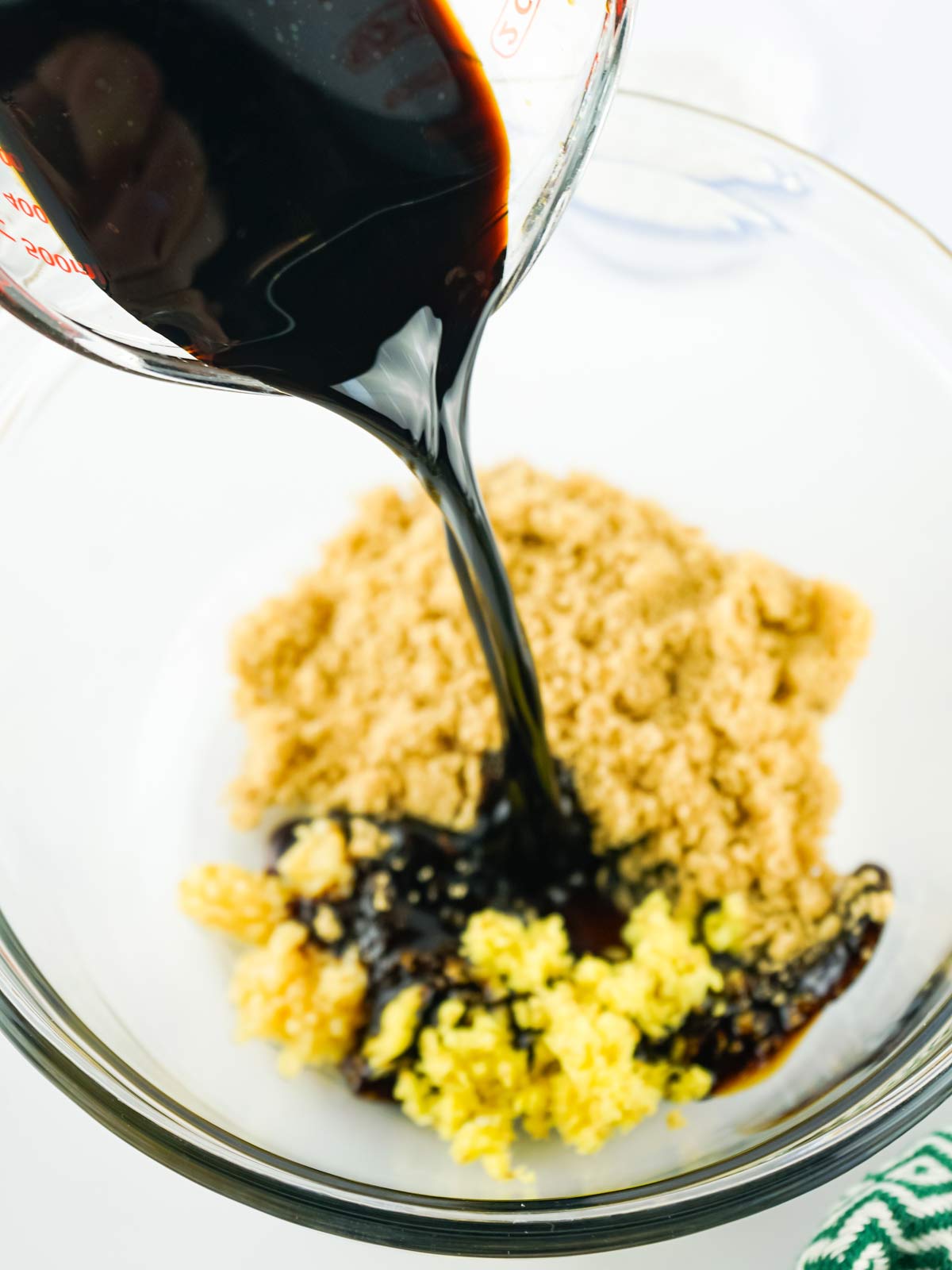 Dark liquid being poured in the bowl with the brown sugar and aromatics.
