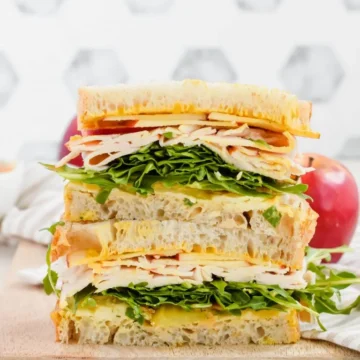 A stack of turkey sandwiches on a wooden cutting board.