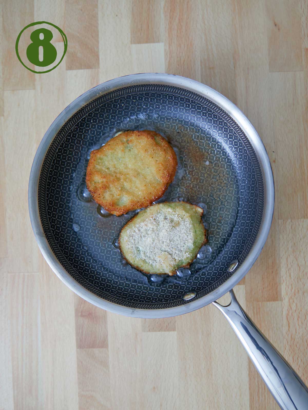 A frying pan with two fried green tomatoes in it prepared using a fried green tomato recipe.