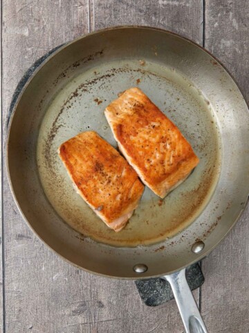 Golden brown skin side up salmon fillets in the saute pan.
