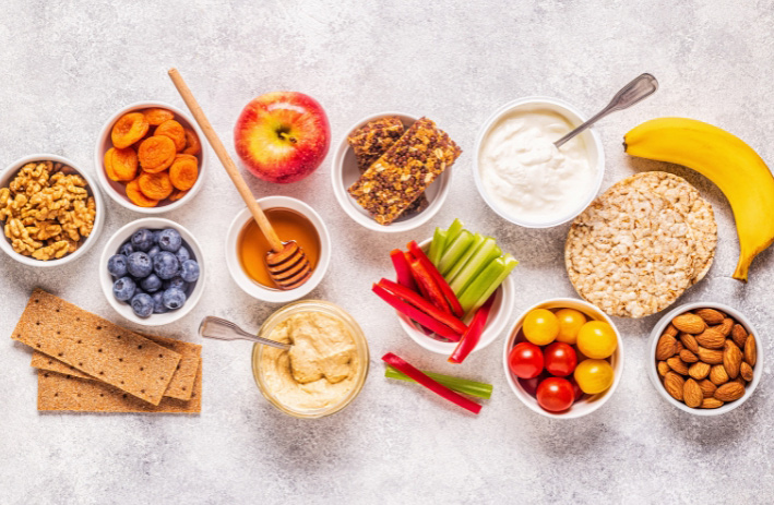 A variety of healthy snacks in bowls on a gray background.