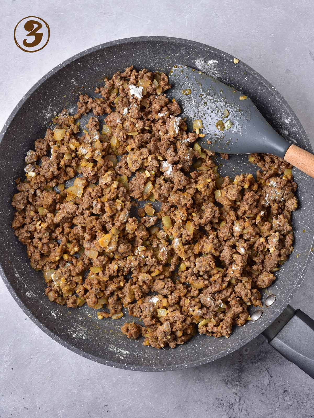 Ground beef in a frying pan with a wooden spoon.