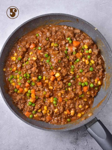 A frying pan filled with beef, vegetables and peas.