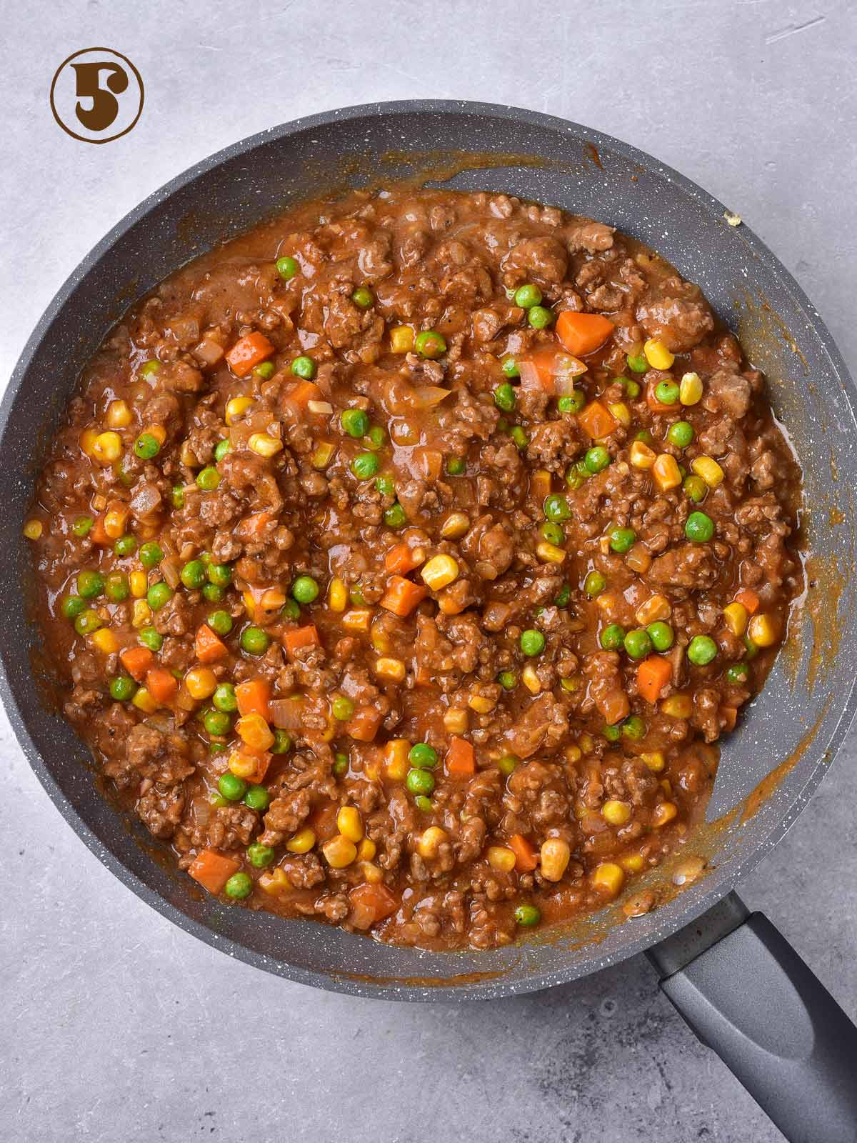 A frying pan filled with beef, vegetables and peas.