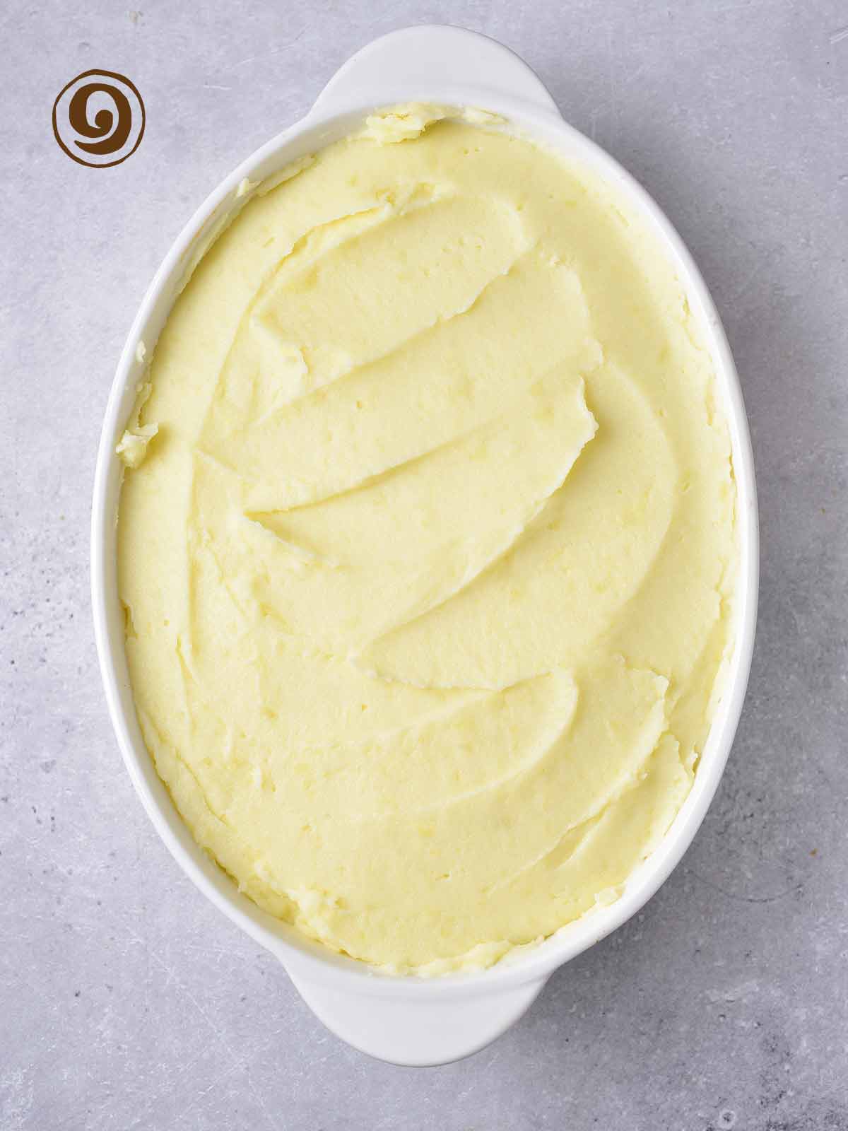 A white dish with mashed potatoes on top of the meat and vegetable mixture.